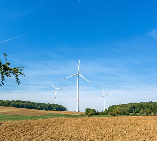 Eine Straße mit Feldern und Windturbinen im Hintergrund, die nachhaltige Energie symbolisieren.