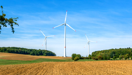 Eine Straße mit Feldern und Windturbinen im Hintergrund, die nachhaltige Energie symbolisieren.